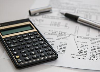 Une calcuatrice et un stylo posés sur un bureau au dessus d'une feuille de calcul