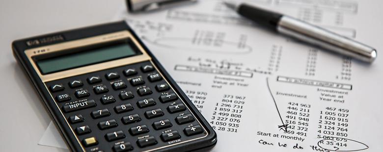 Une calcuatrice et un stylo posés sur un bureau au dessus d'une feuille de calcul